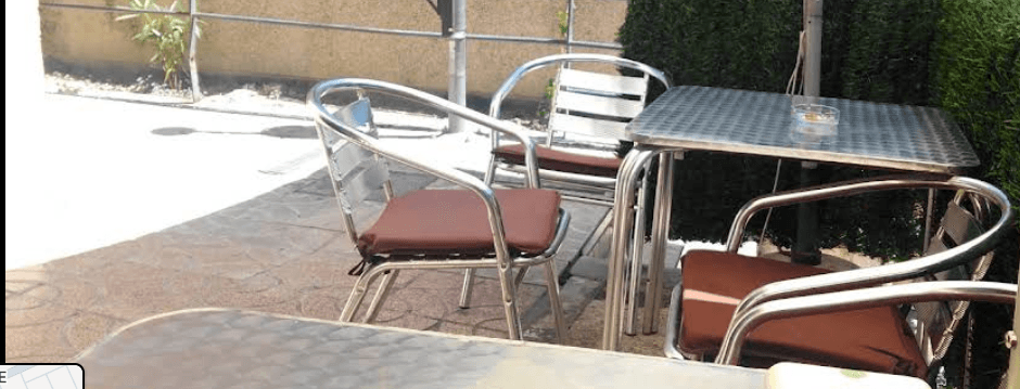 Conjunto de mesa y sillas metálicas con cojines marrones en un patio exterior soleado.