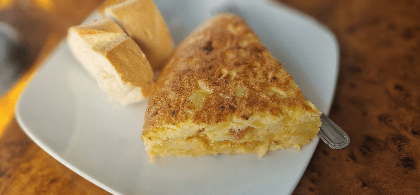 Una porción de tortilla de patatas jugosa servida con dos trozos de pan crujiente.