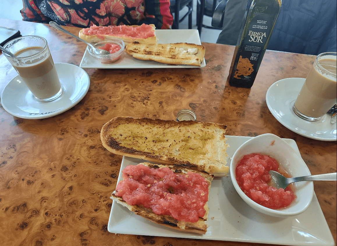 Desayuno de tostadas con tomate y aceite de oliva junto a dos cafés con leche.