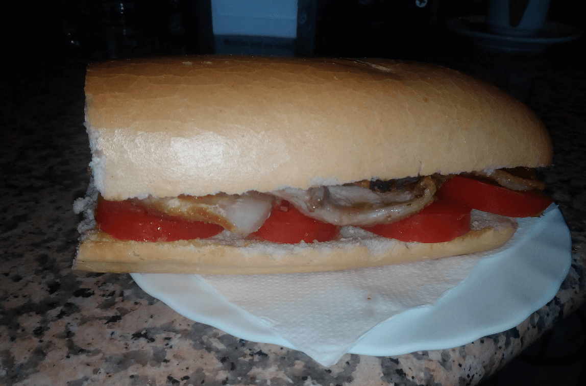 Bocadillo de lomo con tomate en pan crujiente servido sobre un plato con servilleta.