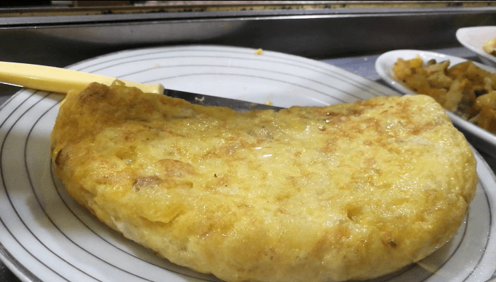 Una jugosa tortilla de patatas dorada servida en un plato blanco con círculos concéntricos grises.